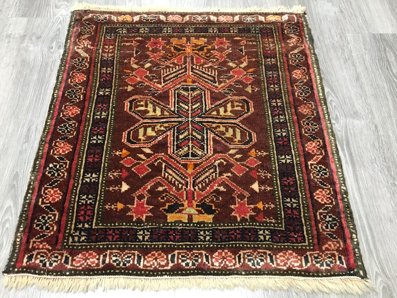 May include: A traditional rug with a dark red background and intricate geometric patterns in shades of red, orange, yellow, green, and black. The rug has a fringe border.