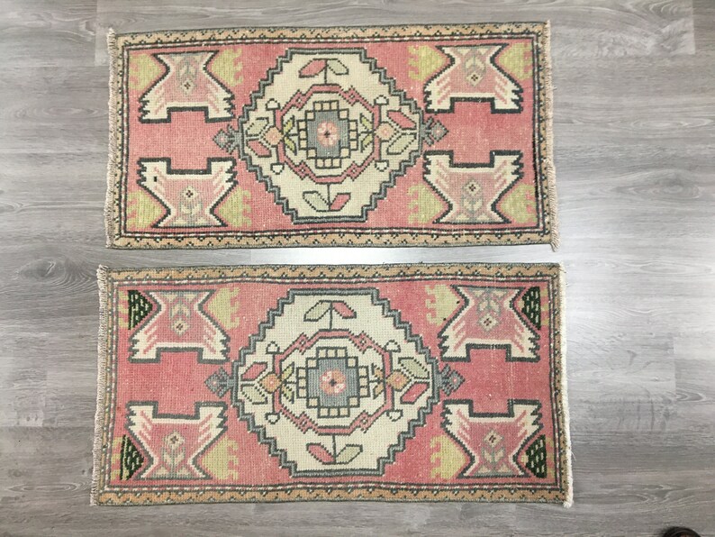 May include: Two pink and cream patterned rugs with intricate geometric designs. The rugs have a fringed edge and are made of a soft, woven material.