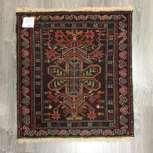 May include: A vintage Turkish rug with a dark red background and intricate floral patterns in shades of green, red, and blue. The rug has a fringe border and is approximately 2 feet by 3 feet.