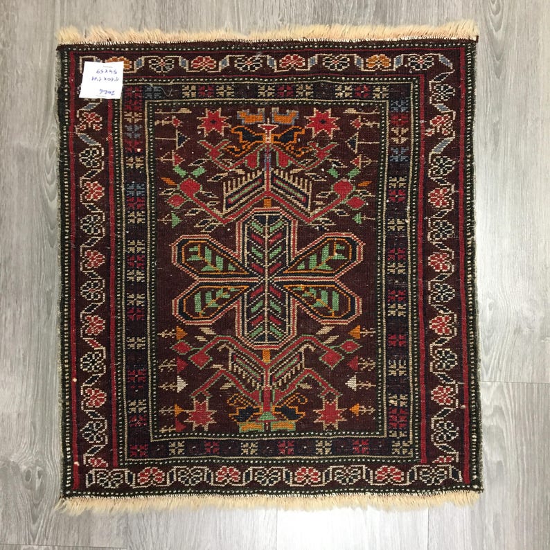 May include: A vintage Turkish rug with a dark red background and intricate floral patterns in shades of green, red, and blue. The rug has a fringe border and is approximately 2 feet by 3 feet.