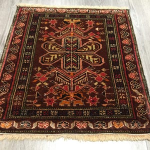 May include: A traditional Turkish rug with a dark red background and intricate geometric patterns in shades of red, orange, yellow, and green. The rug has a fringe border.