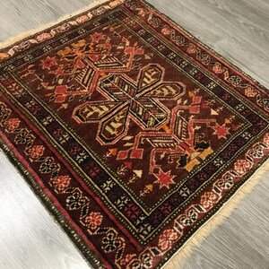 May include: A traditional rug with a geometric pattern in shades of red, brown, green, and cream. The rug has a fringe border and is made of wool.