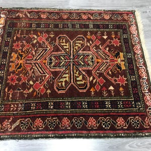 May include: A traditional Turkish rug with a dark red background and intricate floral patterns in shades of orange, yellow, and green. The rug has a fringed border and is woven with a high-quality wool.