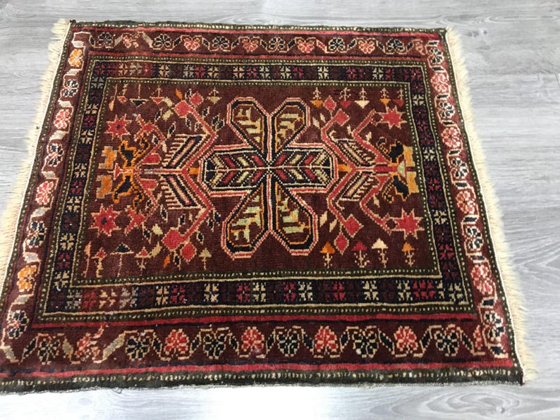 May include: A traditional Turkish rug with a dark red background and intricate floral patterns in shades of orange, yellow, and green. The rug has a fringed border and is woven with a high-quality wool.
