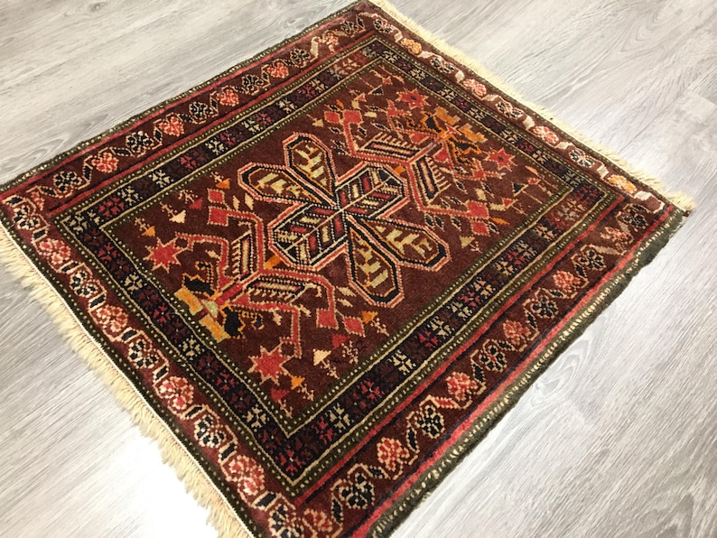 May include: A traditional rug with a brown background and a central design featuring a large, intricate floral motif in shades of red, orange, and yellow. The rug has a fringed border in a cream color.