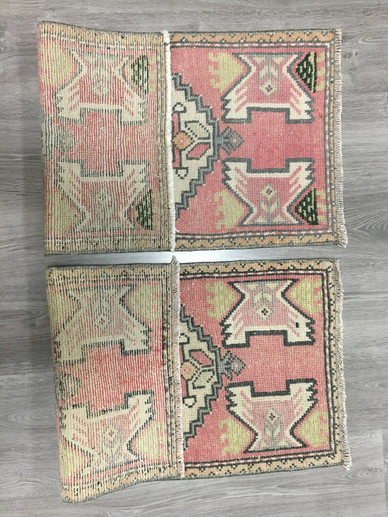 May include: Two pink and cream colored vintage Turkish kilim rugs with geometric patterns. The rugs are folded in half and have fringe on the ends.