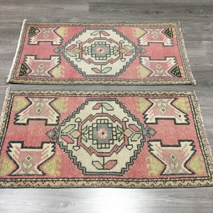 May include: Two pink and cream patterned rugs with intricate designs. The rugs have a fringed edge and are made of a soft, woven material.