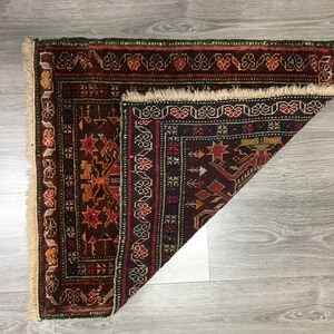 May include: A folded, dark red, black, and cream colored rug with intricate geometric patterns. The rug has a fringe border.