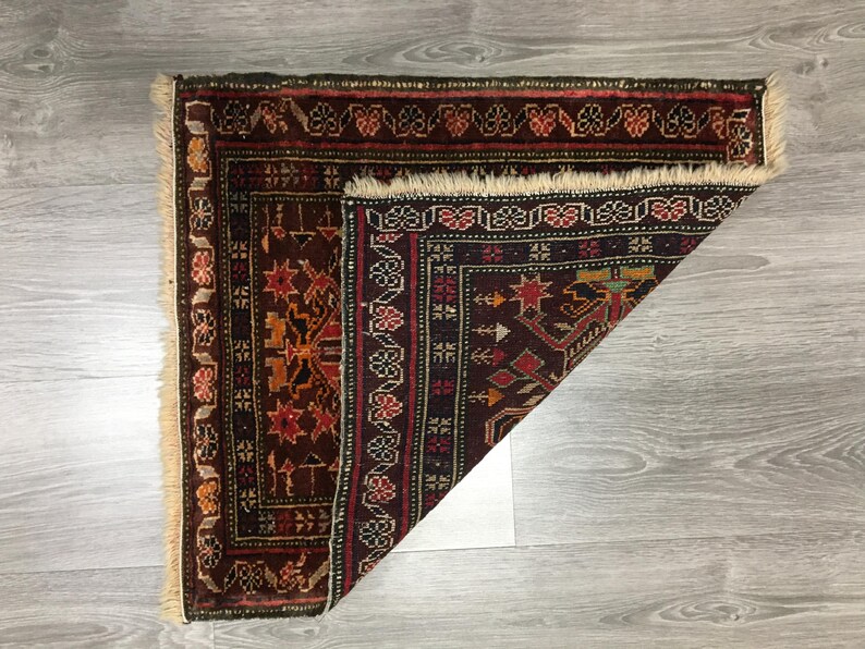 May include: A folded, dark red, black, and cream colored rug with intricate geometric patterns. The rug has a fringe border.
