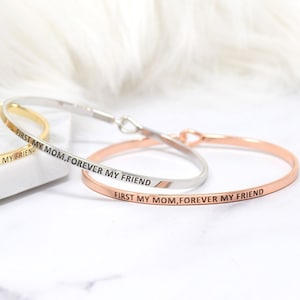 May include: Three bangle bracelets with the inscription "First my mom, forever my friend". The bracelets are in silver, gold, and rose gold.