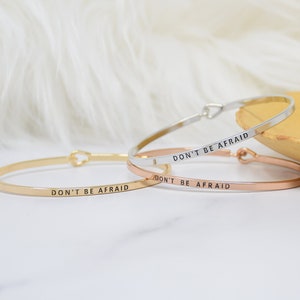 May include: Three delicate gold, rose gold, and silver bangle bracelets with the inscription "Don't be afraid" on each.