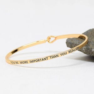 May include: Gold bangle bracelet with the inscription "You're more important than you realize".