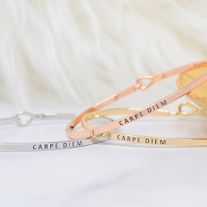 Może przedstawiać: Trzy delikatne bransoletki w kolorze złotym, srebrnym i różowym złocie z napisem "Carpe Diem" na każdej.