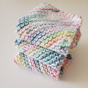 May include: A stack of three knitted dishcloths in a rainbow color pattern of pink, blue, green, and yellow.