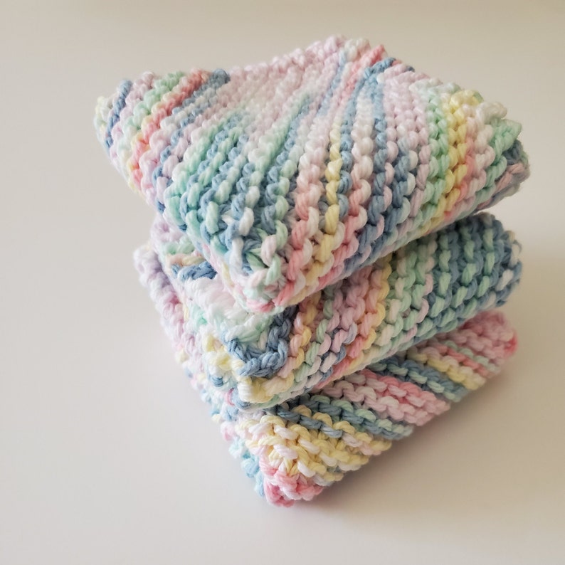 May include: A stack of three knitted dishcloths in pastel colors, including pink, blue, yellow, and green. The dishcloths are made with a textured stitch and have a soft, absorbent feel.