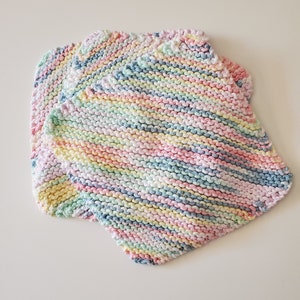 May include: Three multi-colored knitted dishcloths in pastel shades of pink, blue, yellow, and green. The dishcloths are made with a striped pattern.