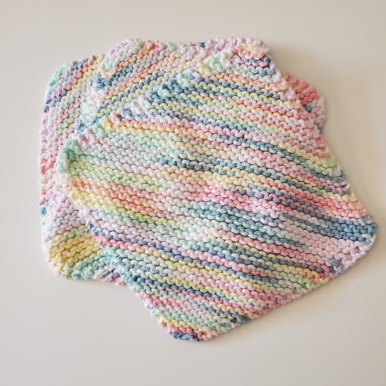 May include: Three multi-colored knitted dishcloths in pastel shades of pink, blue, yellow, and green. The dishcloths are made with a striped pattern.
