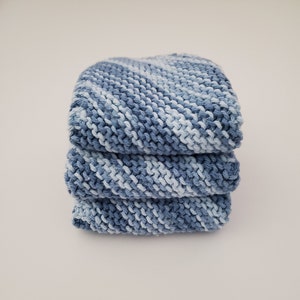 May include: A stack of three blue and white striped knitted dishcloths. The dishcloths are made of cotton yarn and have a soft, absorbent texture.
