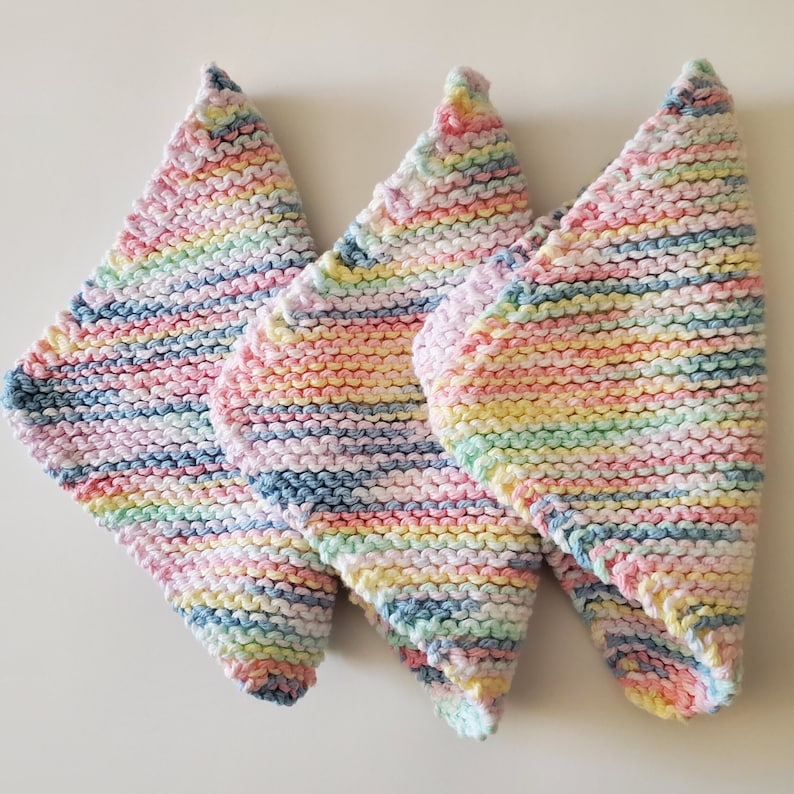 May include: Three knitted dishcloths in a rainbow stripe pattern. The dishcloths are made of cotton yarn and are soft and absorbent.