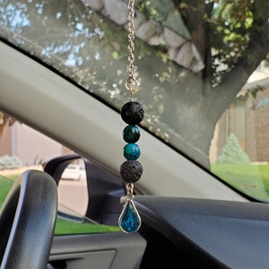 May include: A car charm with a silver chain and a teardrop-shaped blue crystal. The charm also features black lava rock beads and turquoise beads.