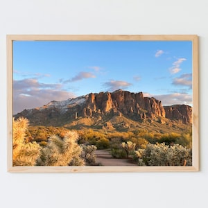 May include: A panoramic view of a mountain range with snow-capped peaks in the distance. The mountains are a reddish-brown color and are surrounded by a lush green landscape. The sky is a clear blue with white clouds.
