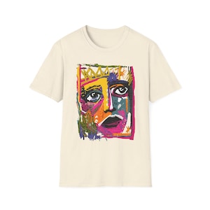 Könnte beinhalten: Cremefarbenes T-Shirt mit einem farbenfrohen abstrakten Gesichtsdesign. Das Kunstwerk zeigt eine gelbe Krone und ein Gesicht mit blauen Augen, einem rosa Mund und orangefarbenen, lila und grünen Akzenten. Das T-Shirt hat kurze Ärmel und einen Rundhalsausschnitt.