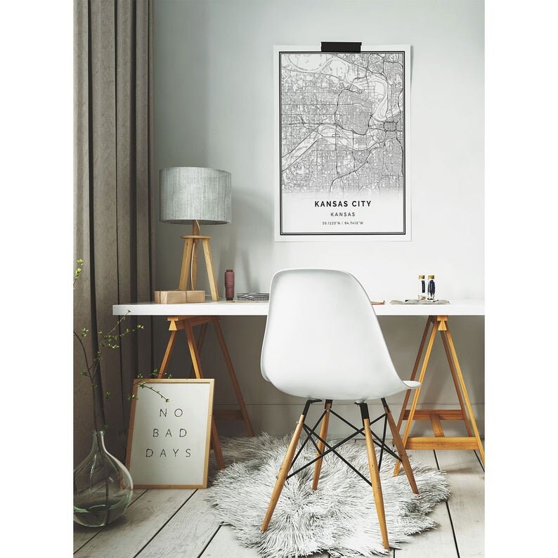 May include: A modern home office setup featuring a white desk, a white chair with wooden legs, and a framed map of Kansas City. A gray lamp and a framed print with the words "NO BAD DAYS" add to the decor.