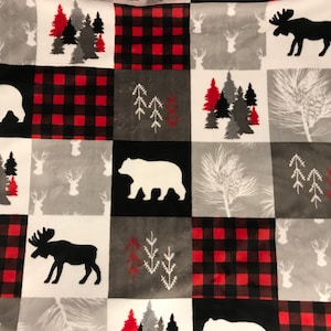 May include: A white, red, and black flannel blanket with a patchwork design featuring bears, moose, and pine trees.