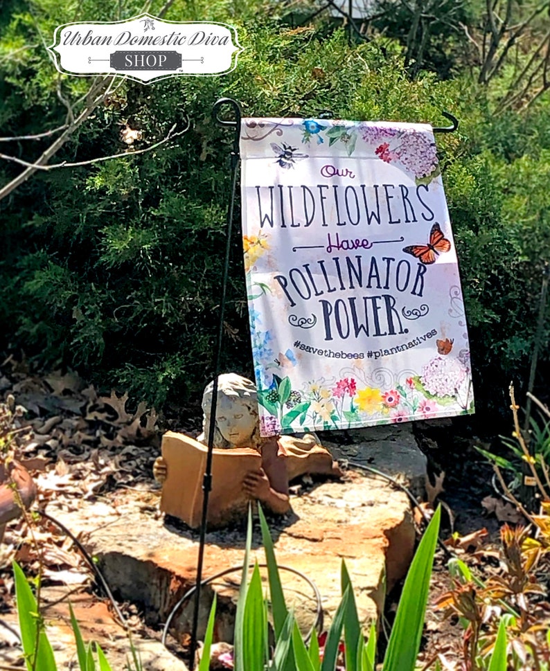 May include: A white garden flag with a floral design and the text "Our Wildflowers Have Pollinator Power. #savethebees #plantnatives".
