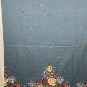 May include: A dusty blue fabric featuring a scattered pattern of small red rosebuds across the top section and a dense, horizontal border at the bottom displaying large, multi-colored floral bouquets in shades of yellow, red, and blue.