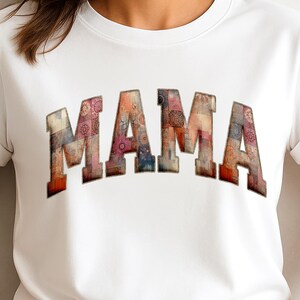 May include: White t-shirt featuring the word "MAMA" in large, textured letters. The letters are designed with a patchwork pattern in shades of red, pink, and blue. The shirt has short sleeves.