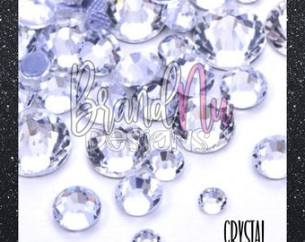 May include: A close-up image of clear crystal rhinestones. The rhinestones are scattered on a white surface. The word "CRYSTAL" is printed in black at the bottom of the image.