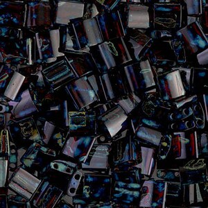 Puede incluir: Primer plano de un montón de cuentas de vidrio azul oscuro y negro con acentos iridiscentes. Las cuentas son rectangulares y tienen una forma ligeramente curvada.