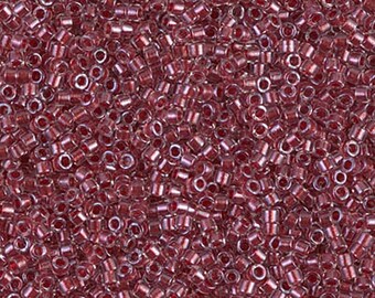 May include: A collection of small, cylindrical glass seed beads in a deep, translucent cranberry red color. Each bead features a consistent tubular shape with a central hole, creating a uniform texture across the entire surface of the pile.