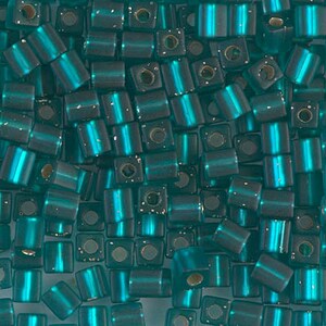 May include: Teal blue square seed beads with a metallic sheen. The beads have a slightly iridescent finish.