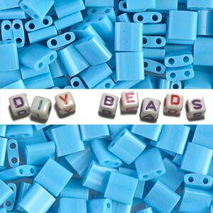 May include: A large quantity of light blue plastic beads with two holes in each bead. The beads are arranged in a random pattern. The words "DIY BEADS" are spelled out in white letter beads with colorful letters.