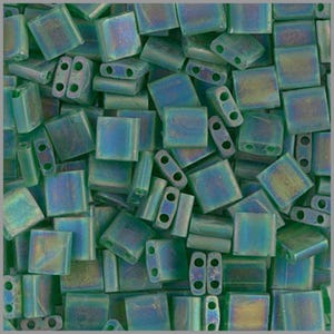 May include: A close-up of a pile of small, square, green iridescent glass beads. The beads have two holes in each.