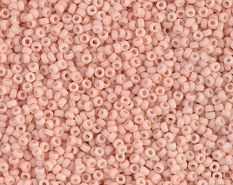 May include: A large collection of small, round, matte-finish beads in a uniform pale blush pink color. Each bead features a central hole, creating a consistent, textured pattern across the entire surface of this dense arrangement of craft supplies.