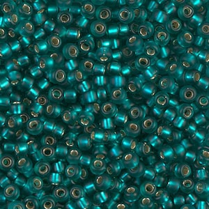 May include: A close-up view of teal blue seed beads. The beads are small and round, with a slightly iridescent finish.