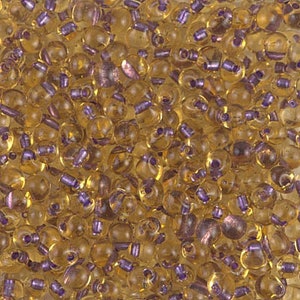 May include: A close-up of a large quantity of small, round, translucent amber glass beads with a purple iridescent sheen.