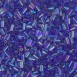 May include: A close-up view of a large quantity of iridescent blue glass seed beads. The beads are cylindrical in shape and have a metallic sheen.
