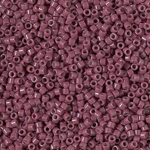 May include: A close-up image of a large quantity of small, round, opaque, mauve-colored glass beads.
