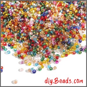 Peut inclure: Une grande collection de petites perles de rocaille rondes et translucides dans un m&eacute;lange vibrant de couleurs incluant rouge, bleu, vert, jaune, orange, violet et transparent. Les perles sont &eacute;parpill&eacute;es sur un fond blanc avec le texte diyBeads.com.
