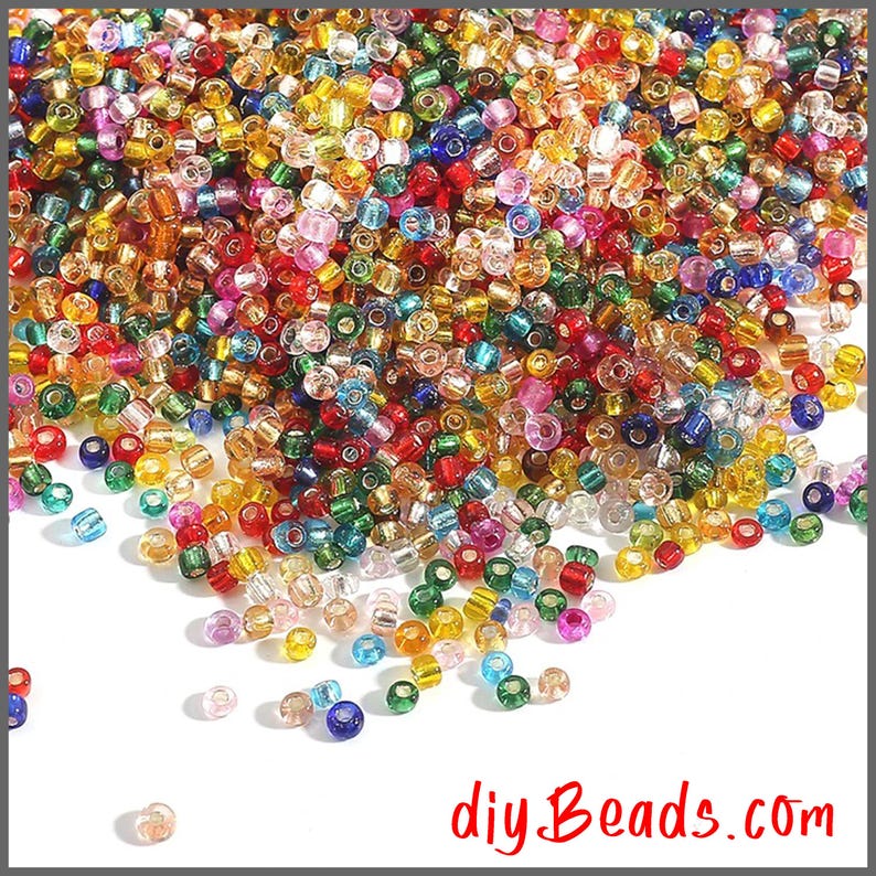 Peut inclure: Une grande collection de petites perles de rocaille rondes et translucides dans un m&eacute;lange vibrant de couleurs incluant rouge, bleu, vert, jaune, orange, violet et transparent. Les perles sont &eacute;parpill&eacute;es sur un fond blanc avec le texte diyBeads.com.