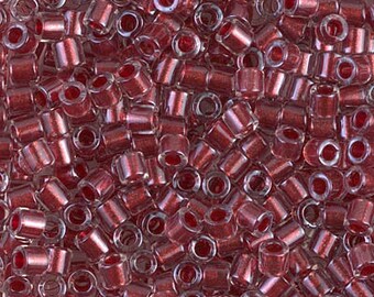 May include: A close-up view of a large quantity of small, transparent red glass beads with a metallic sheen. The beads are cylindrical in shape with a hole through the center.