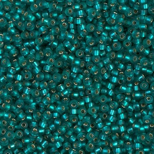 May include: A close-up image of a large quantity of teal seed beads. The beads are small and round, with a slightly iridescent finish.