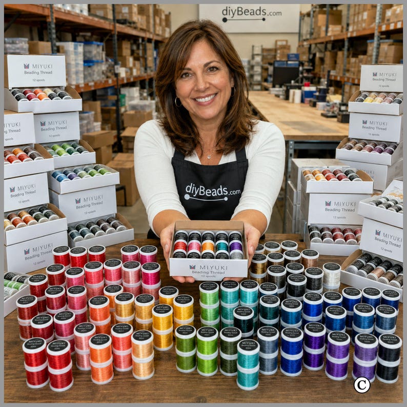 May include: A collection of Miyuki beading thread spools in various colors, including red, orange, yellow, green, blue, and purple. The spools are arranged in white boxes, with one box held in the center, and many others stacked on a wooden surface.