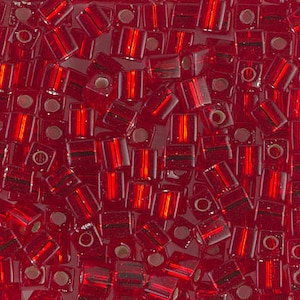 May include: Close-up of a pile of small, translucent red glass beads. The beads are rectangular with a square hole running through the center. The beads have a reflective, glossy finish, and are scattered randomly.