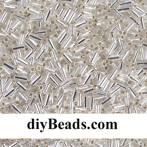 May include: A close-up image of a large quantity of small, clear glass beads. The beads are cylindrical in shape and have a silver metallic finish. The beads are scattered randomly across the image.