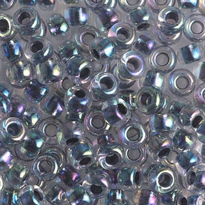 May include: A close-up of a pile of iridescent silver seed beads. The beads are small and round, with a hole in the center. They have a subtle shimmer and a slightly translucent appearance.